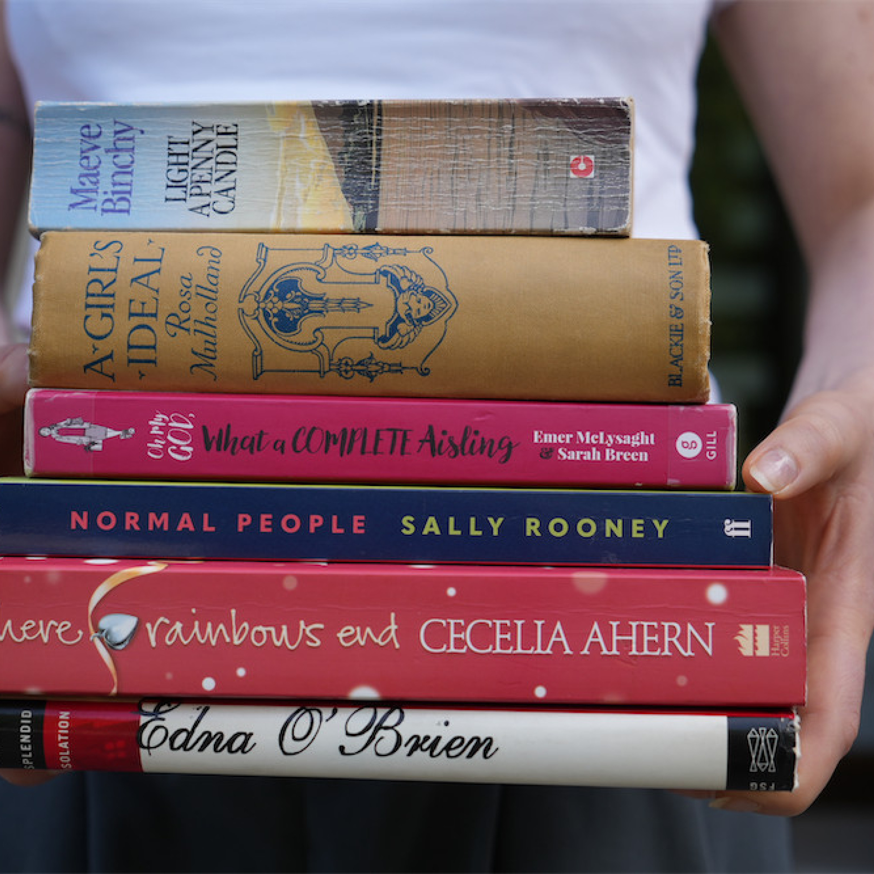 Photograph of a person holding a stack of romance novels.