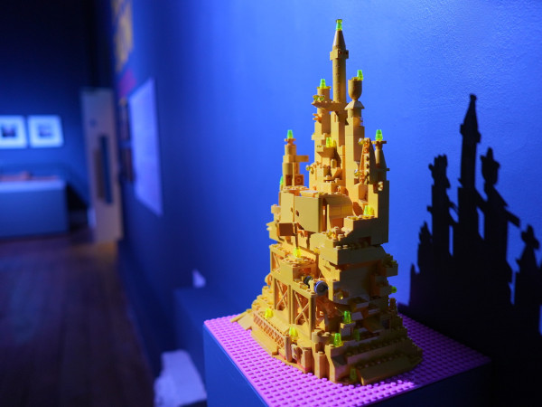 Photograph of an artpiece made of yellow building blocks against a blue background.