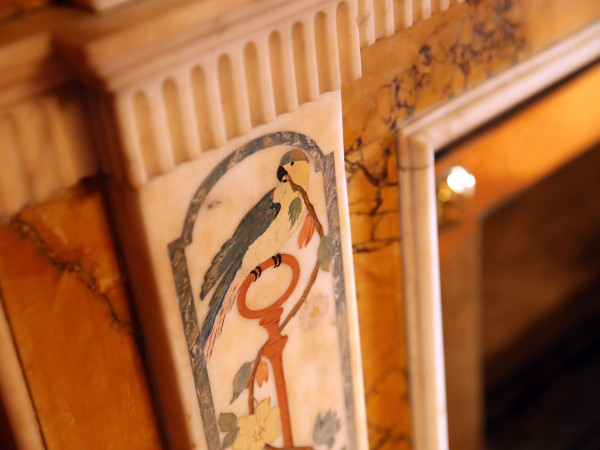 Photograph of a detail on a fireplace, depicting a bird upon a key with a branch in its mouth.