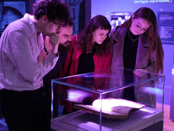 Photograph of four people looking at a manuscript in a glass case.